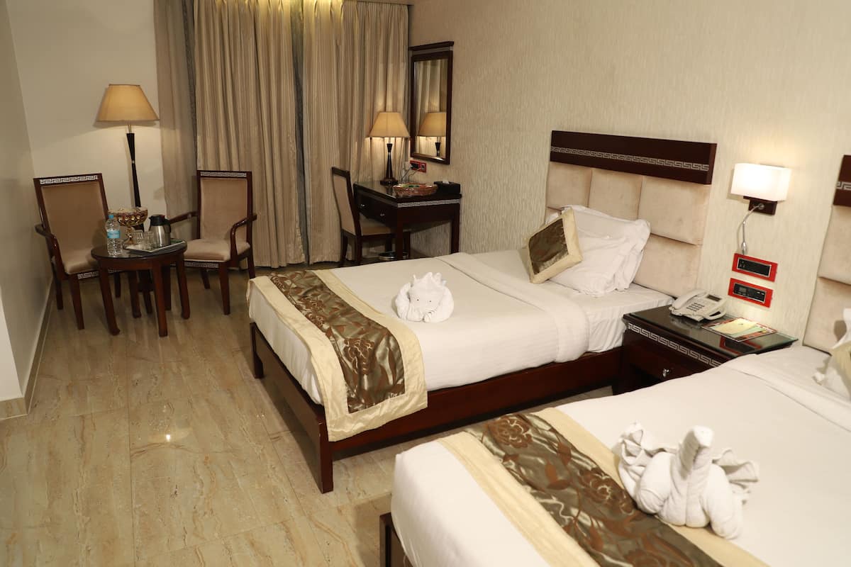 A hotel room with two beds, a desk with a lamp, a chair, and a bedside table with a phone.