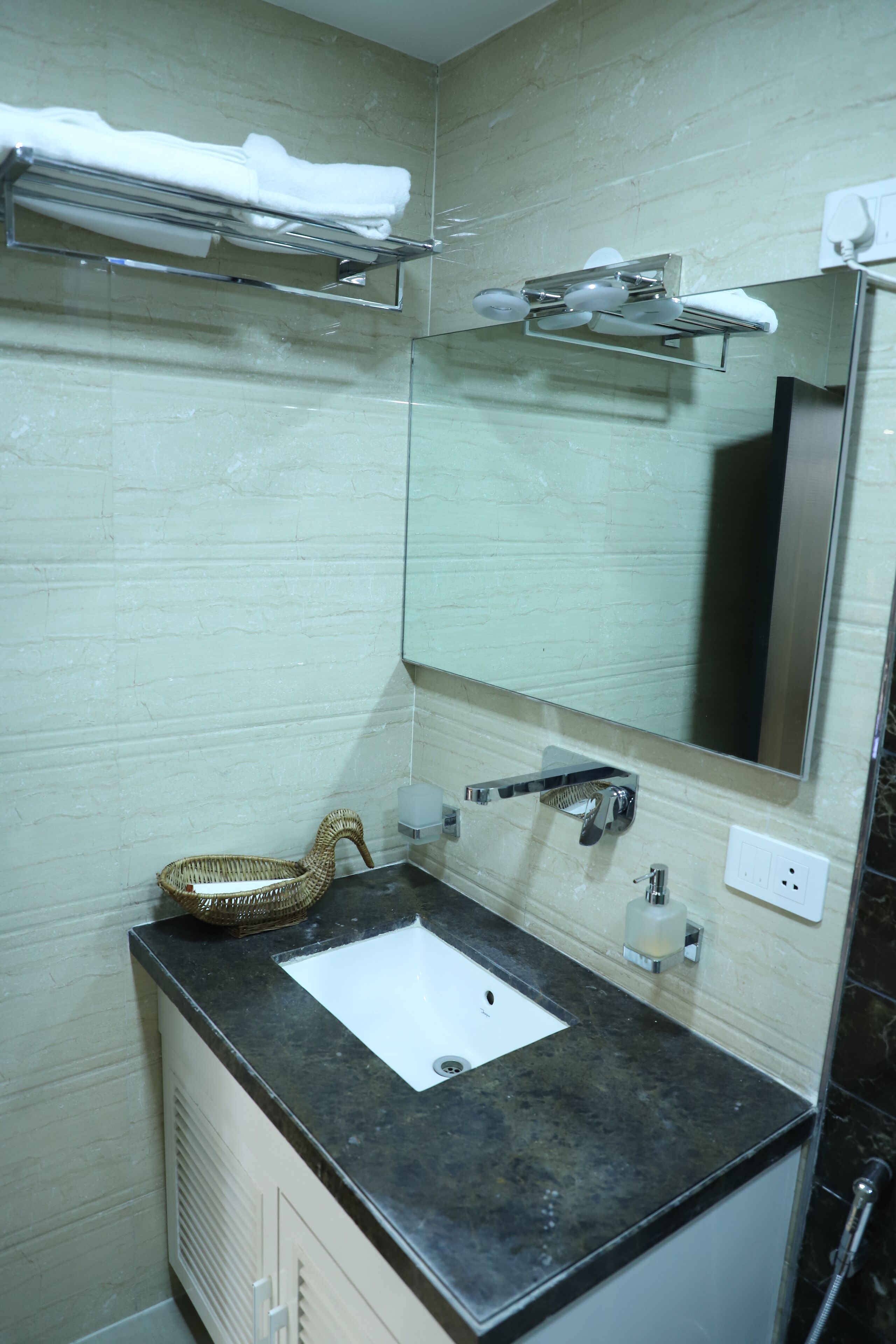 Un baño con un lavamanos blanco, un espejo, un perchero y una cesta.