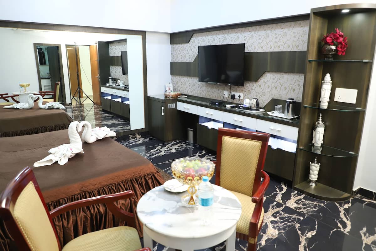 A hotel room with a dining area, a TV mounted on the wall, a minibar, and a decorative shelf with a statue.