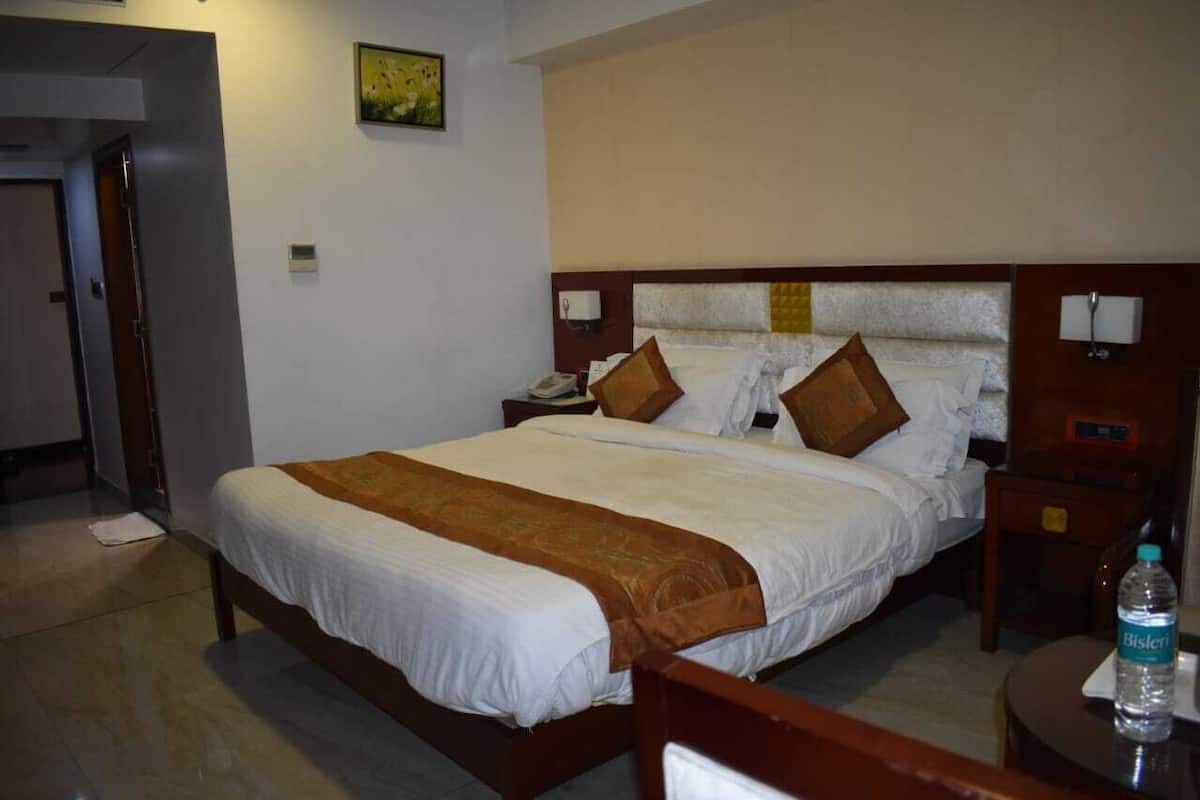 A hotel room with a large bed, a nightstand, a bedside table, and a water bottle on the nightstand.