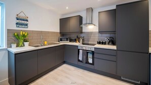 A modern kitchen with dark cabinetry, a stainless steel range hood, a built-in microwave, and a kettle on the countertop. - Windmill House Apartment 4 (Lytham Saint Annes)