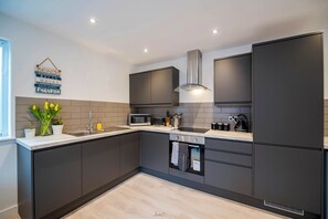Una cucina moderna con mobili scuri, una cappa aspirante in acciaio inox, un forno a microonde integrato e un bollitore sul piano di lavoro.