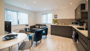 A modern kitchen with a microwave, sink, and stove. There is a dining area with a table and chairs. - Windmill House Apartment 4 (Lytham Saint Annes)