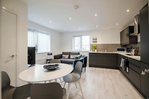 Une cuisine moderne avec des meubles de couleur sombre, un plan de travail blanc et un coin repas comprenant une table ronde et des chaises.