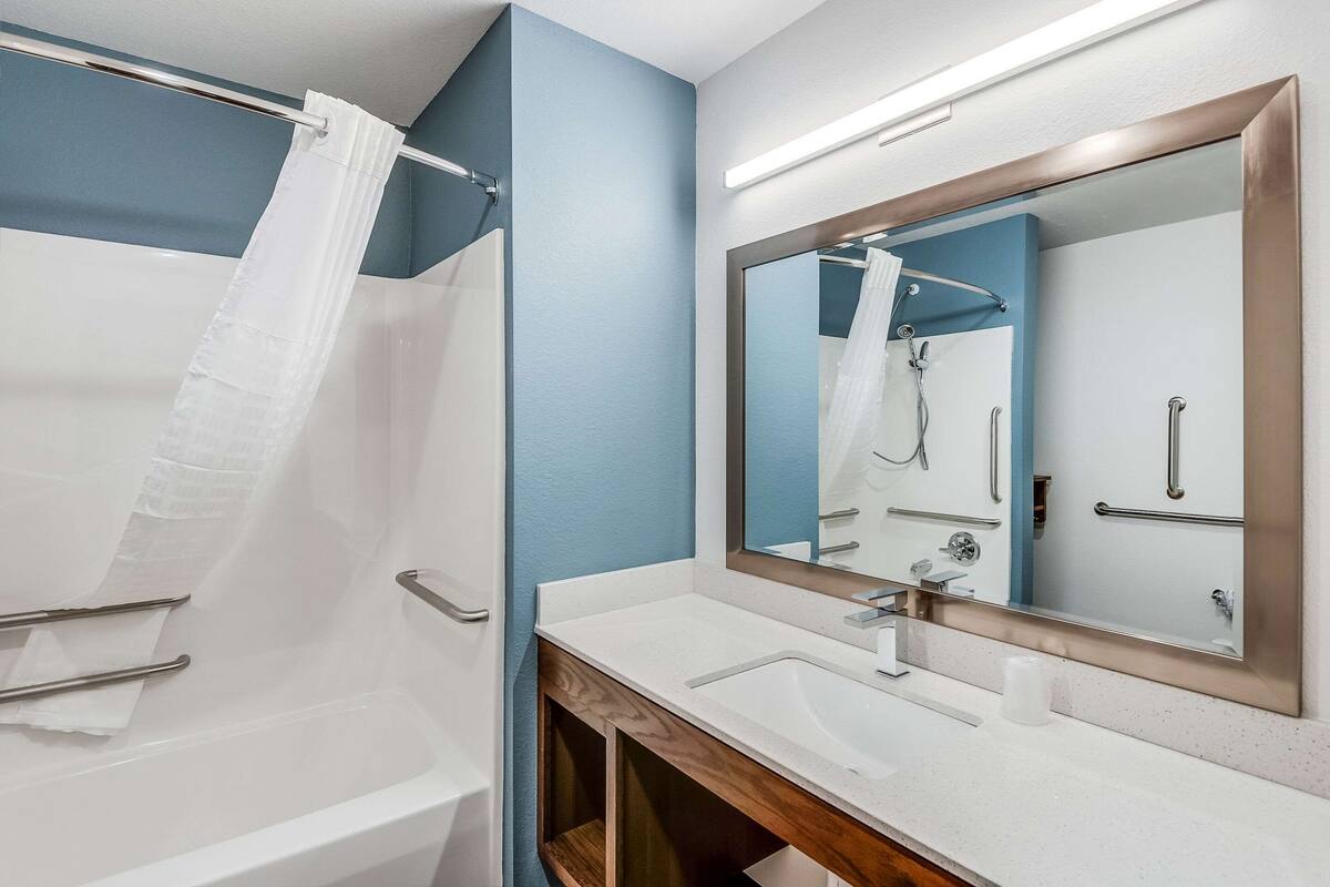 A modern bathroom with a bathtub, a large mirror, and a vanity with a sink.