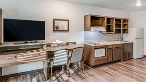 A modern kitchen with a built-in TV, wooden cabinets, a microwave, and a refrigerator. - Woodspring Suites  West Des Moines (West Des Moines)