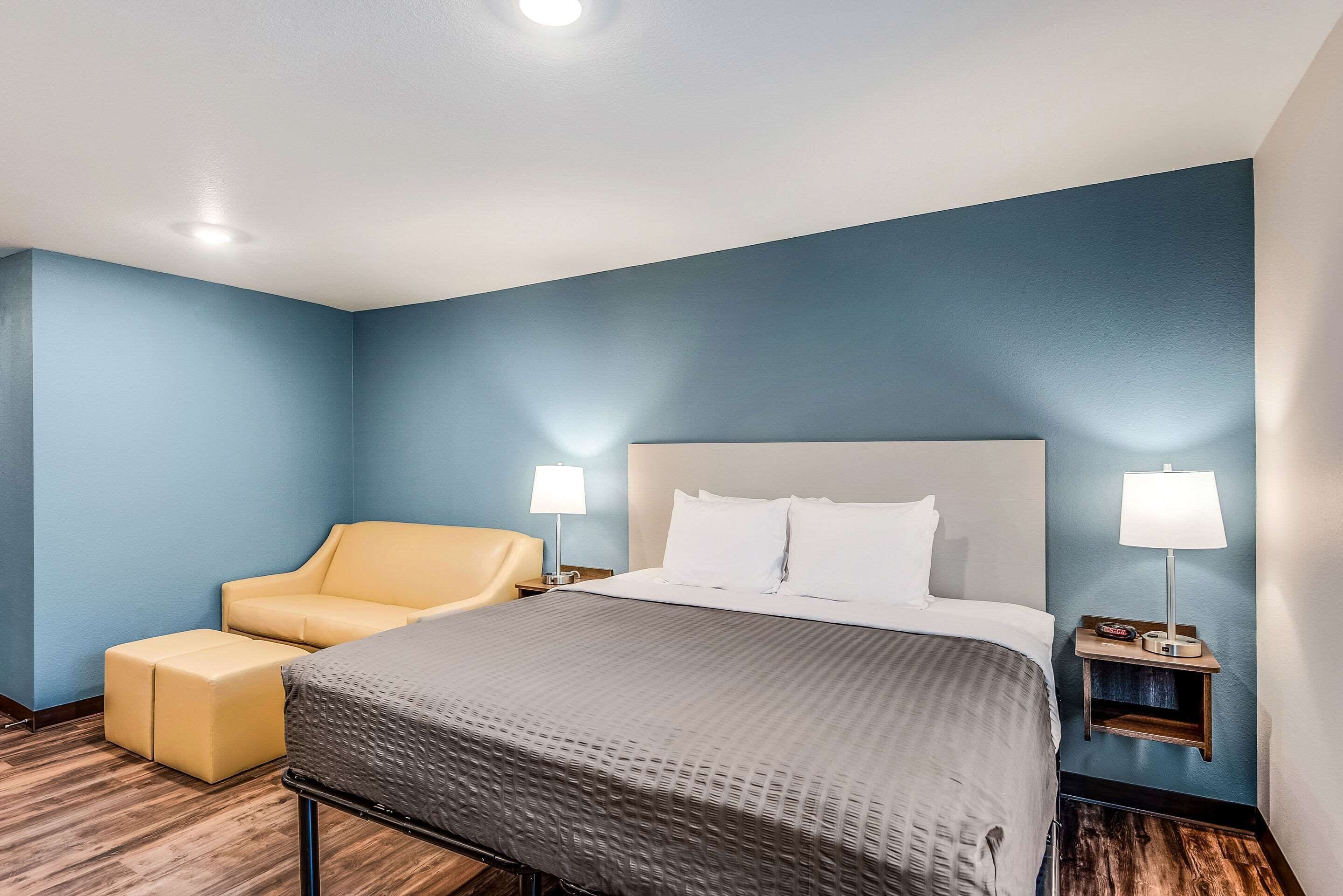 A hotel room with a bed, a chair, two bedside lamps, and a nightstand.