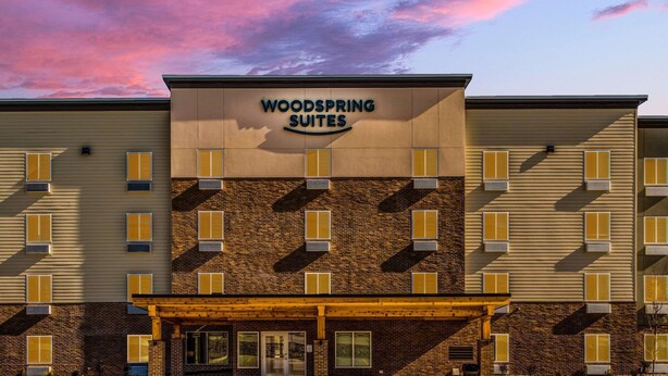 A hotel with a sign reading "WOODSPRING SUITES" and a brick facade. - Woodspring Suites  West Des Moines (West Des Moines)