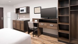 A modern hotel room with a bed, a desk with a computer, a microwave, a TV, and built-in shelving. - Woodspring Suites  West Des Moines (West Des Moines)