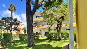 A courtyard with a large tree, well-maintained grass, and a building with balconies. - Nautilus A (Quarteira)