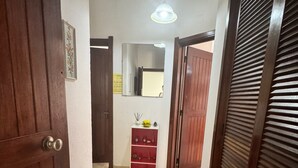 A hallway with a wooden door, a mirror, a shelf with decorative items, and a ceiling light. - Nautilus A (Quarteira)