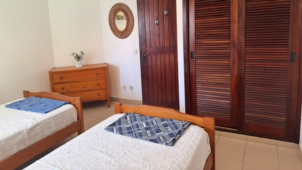 A bedroom with two wooden beds, a wooden dresser, a wooden wardrobe, and a wall-mounted mirror. - Nautilus A (Quarteira)