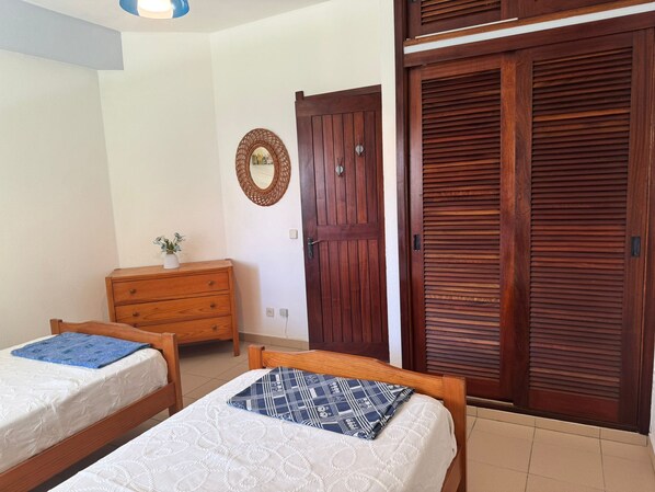 A bedroom with two wooden beds, a wooden dresser, a wooden wardrobe, and a wall-mounted mirror.