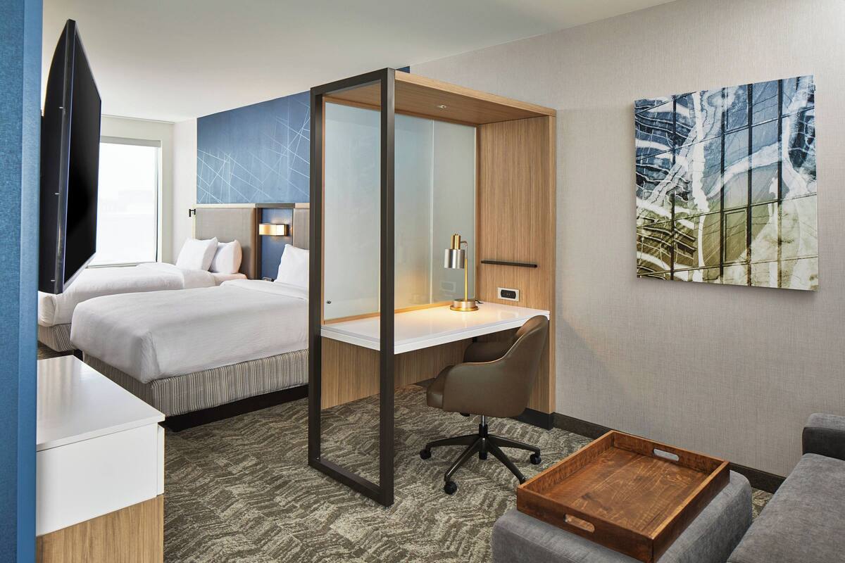 A hotel room with a bed, a desk, a chair, a TV, and a painting on the wall.
