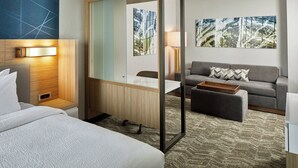 A hotel room with a bed, a desk, a sofa, and a large mirror.