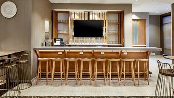Eine moderne Bar mit Holzhockern, einem Flachbildfernseher und Regalen mit Gläsern.