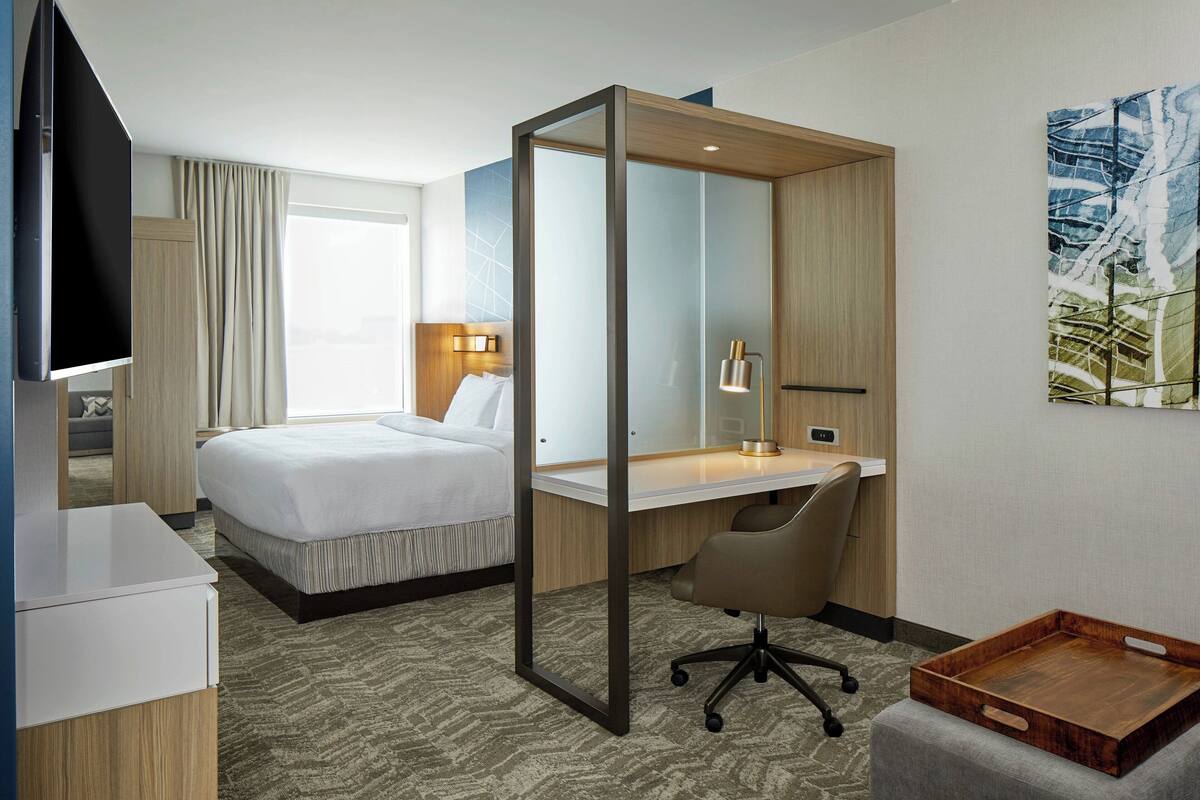 A hotel room with a bed, desk, chair, and a TV.