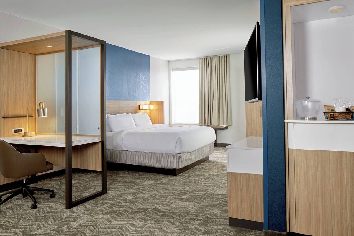 A hotel room with a bed, a desk, a chair, a TV, and a bathroom.