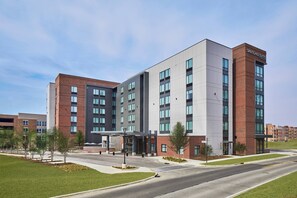 Ett modernt hotell med flera våningar, en inglasad entré och en välskött gräsmatta.