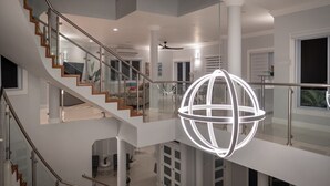 Ein modernes Interieur mit einer gläsernen Wendeltreppe, einer kugelförmigen Leuchte und Blick ins Wohnzimmer darunter.