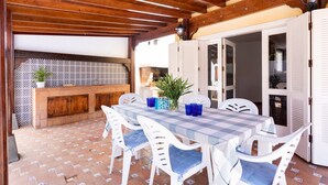 Une terrasse extérieure avec une table à carreaux, des chaises blanches et un plafond en bois.