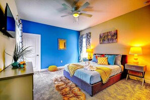 A bedroom with a bed, bedside lamps, a ceiling fan, a door, and a wall-mounted TV. - Secret Cove (Davenport)
