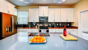 A modern kitchen with white cabinets, stainless steel appliances, and a central island with a bowl of oranges and a wine bottle. - Secret Cove (Davenport)
