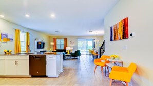 Une cuisine moderne dotée d’un îlot central, un coin repas avec des chaises orange et un espace de vie comprenant un canapé et une table basse.