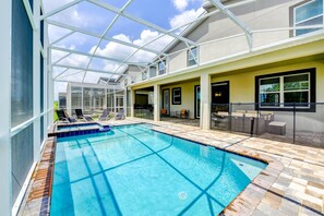 A swimming pool with a glass ceiling, lounge chairs, and a patio area.