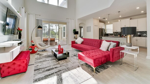 A spacious living area with a red sectional sofa, a flat-screen TV, and a modern kitchen in the background. - Ruby Falls Villa (Kissimmee)