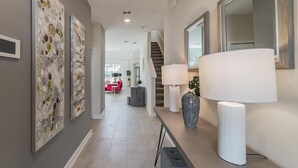A modern hallway with artwork on the walls, a staircase, and a seating area in the background. - Ruby Falls Villa (Kissimmee)