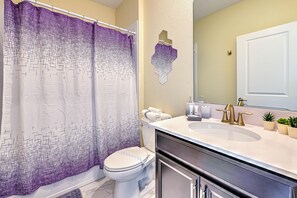 A bathroom with a shower curtain, toilet, sink, and mirror. - Blooming Villa (Kissimmee)