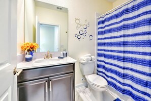 A bathroom with a white toilet, a sink with a mirror, and a shower curtain with a blue and white striped pattern. - Blooming Villa (Kissimmee)