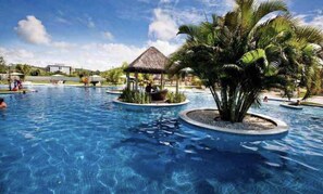 A swimming pool with palm trees and a thatched-roof structure. - Iloa Resort, a paradise waiting for you. (Barra de São Miguel)