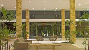 Un moderno vestíbulo con zona de estar, ventanas amplias y plantas tropicales.