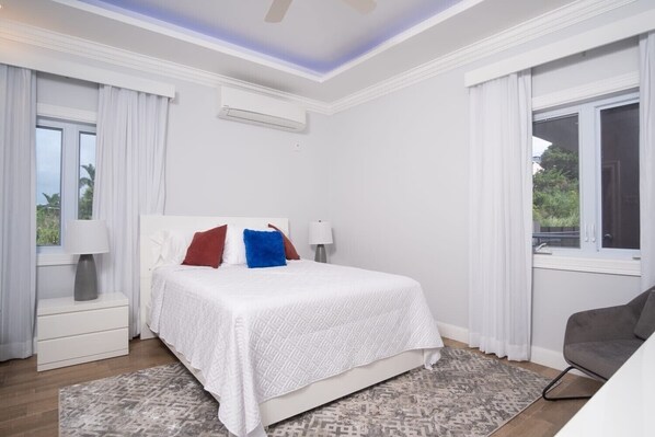 A bedroom with a bed, bedside tables, a lamp, a chair, and a window. - The Sun Seeker Villa Ja. 5 Bedrooms in Montego Bay. Fully staffed. (Montego Bay)
