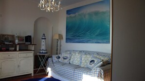 A room with a checkered sofa, a chandelier, a painting of a wave, a lighthouse model, and a cabinet. - Apartment by the sea (Augusta)