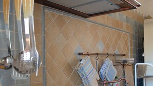 A kitchen with a gas stove, hanging utensils, and a tiled backsplash. - Apartment by the sea (Augusta)