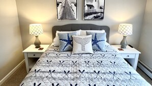 Une chambre à coucher comprenant un lit, deux tables de chevet, deux lampes fixées au mur, une tête de lit et deux tableaux représentant des phares.