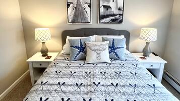 Une chambre à coucher comprenant un lit, deux tables de chevet, deux lampes fixées au mur, une tête de lit et deux tableaux représentant des phares.