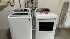 Deux appareils électroménagers blancs superposés, probablement une machine à laver et un sèche-linge, avec un câble d’alimentation visible et un petit récipient placé sur le dessus.