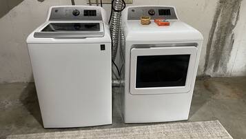 Deux appareils électroménagers blancs superposés, probablement une machine à laver et un sèche-linge, avec un câble d’alimentation visible et un petit récipient placé sur le dessus.