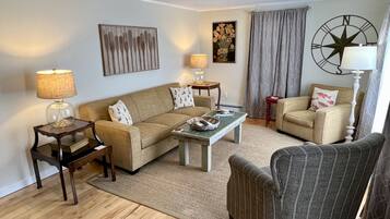 Un salon comprenant un canapé, deux fauteuils, une table basse et une lampe. Un tableau est accroché au mur, et il y a une décoration en forme de boussole.