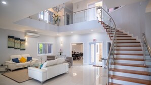 A spacious living area with a high ceiling, a staircase, and a dining area visible in the background.