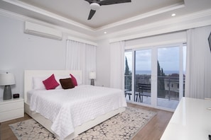 A modern hotel room with a large bed, white bedding, a ceiling fan, and a balcony with a city view.