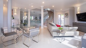 Un vaste espace de vie comprenant une table à manger en verre, des canapés blancs et un escalier menant à l’étage supérieur.