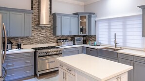 Une cuisine moderne avec des meubles gris, un four encastré, une cuisinière et un grand îlot central.