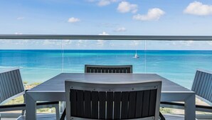 Un balcon avec une table et des chaises donnant sur une mer bleue et limpide, où l’on aperçoit un voilier.
