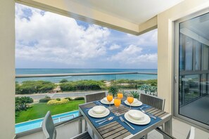 A balcony with a table set for breakfast overlooking a coastal view.