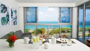 A modern dining area with a table set for breakfast, large windows with a view of the ocean, and tropical artwork on the wall. - Peace and Light, Ocean View Condo on the 5th floor (Eagle Beach)